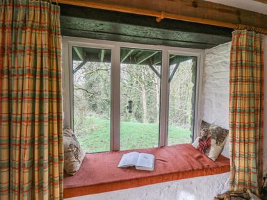 A window seat with cushions and an open book overlooking a garden at Trawsnant Cottage in New Quay Ceredigion