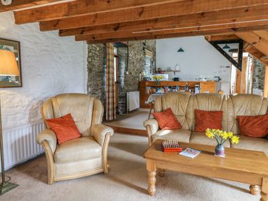 A living room with beige armchairs and sofa with red cushions a wooden coffee table with flowers and a chess board at Trawsnant Cottage in New Quay Ceredigion