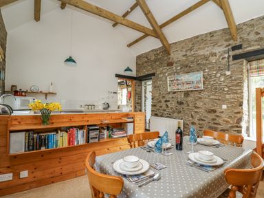 A dining area with a table set for four and a kitchen with wooden shelves and books at Trawsnant Cottage in New Quay Ceredigion