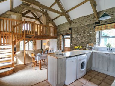 A kitchen and dining area with wooden beams stone walls and a staircase leading to a loft at Trawsnant Cottage in New Quay Ceredigion