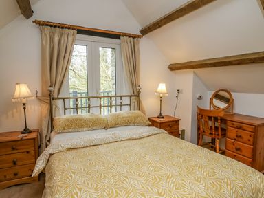 A bedroom with a double bed yellow bedspread wooden bedside tables with lamps and wooden dressing table with chair at Trawsnant Cottage in New Quay Ceredigion