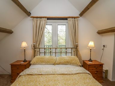 A bedroom with a bed yellow patterned bedding wooden bedside tables and lamps at Trawsnant Cottage in New Quay Ceredigion