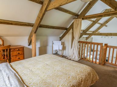 A bedroom with wooden beams a bed a wooden chair and dresser and a railing overlooking a lower level at Trawsnant Cottage in New Quay Ceredigion