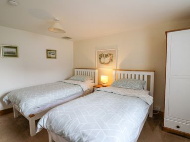 A bedroom with two single beds a nightstand with a lamp a wardrobe and framed pictures on the walls at Trawsnant Cottage in New Quay Ceredigion