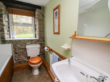 A bathroom with a toilet, sink, bathtub, window, and a framed picture on the wall at Trawsnant Cottage in New Quay Ceredigion