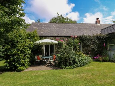A garden with outdoor table and chairs with umbrella and plants at Trawsnant Cottage in New Quay Ceredigion