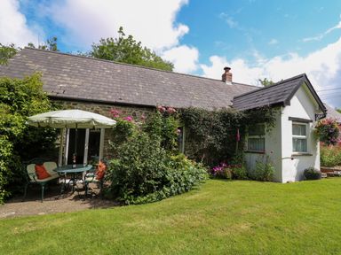 A stone cottage with a slate roof and a garden table with umbrella surrounded by plants at Trawsnant Cottage in New Quay Ceredigion
