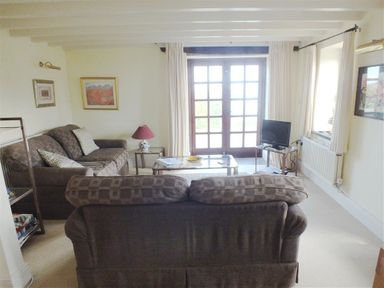 A living room with brown sofas a glass coffee table a television and French doors at Cockshead Cottage St Dogmaels Pembrokeshire