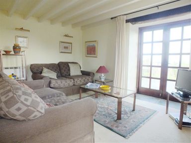 A living room with two sofas a glass coffee table a rug a television and French doors at Cockshead Cottage in St Dogmaels Pembrokeshire