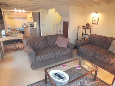 A living room with two sofas a glass coffee table and an open kitchen and dining area at Cockshead Cottage in St Dogmaels Pembrokeshire