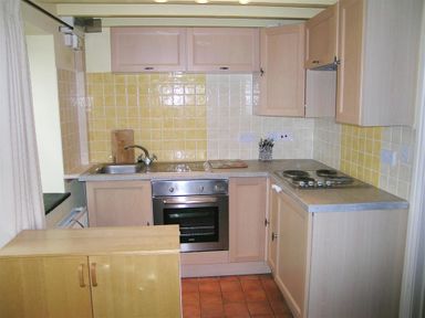 A kitchen with wooden cabinets stainless steel sink electric stove and oven with tiled backsplash at Cockshead Cottage in St Dogmaels Pembrokeshire