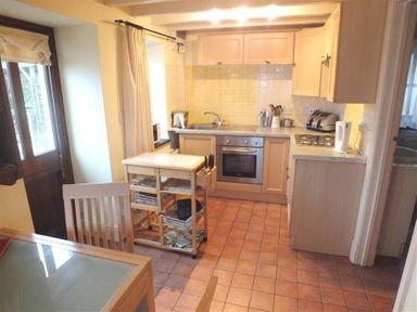 A kitchen with wooden cabinets a metal oven a sink a kettle a toaster and a wooden cart with baskets at Cockshead Cottage in St Dogmaels Pembrokeshire