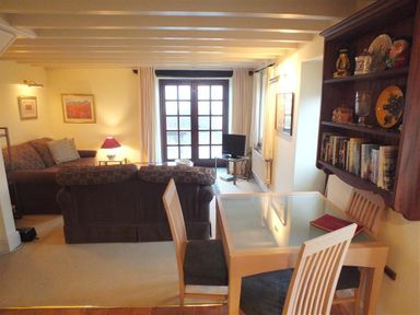 A living room with sofas a glass dining table with chairs a bookshelf and a TV at Cockshead Cottage in St Dogmaels Pembrokeshire