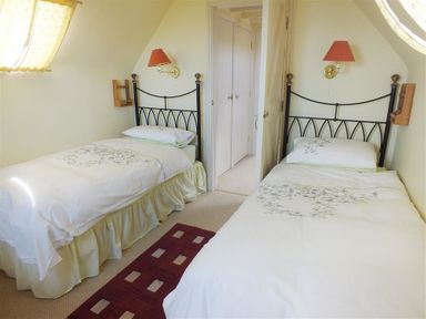 A bedroom with two single beds a maroon rug on the floor and wall lamps at Cockshead Cottage in St Dogmaels Pembrokeshire