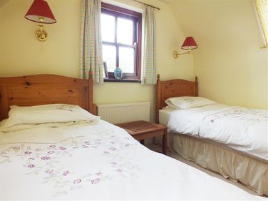 A bedroom with two single beds and a window between at Cockshead Cottage in St Dogmaels Pembrokeshire