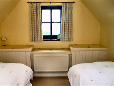 A bedroom with two single beds separated by a radiator below a window with checked curtains at Cockshead Cottage in St Dogmaels Pembrokeshire