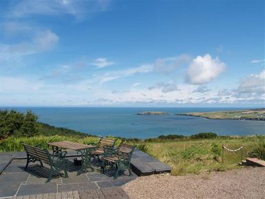 An outdoor seating area with benches and a table overlooking the sea at Cockshead Cottage in St Dogmaels Pembrokeshire
