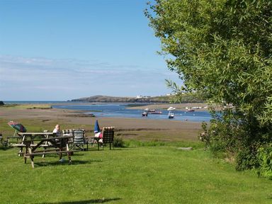 A grassy area with picnic tables and chairs overlooking a river with boats and a distant shoreline at Cockshead Cottage in St Dogmaels Pembrokeshire