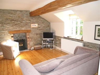 A living room with a grey sofa a armchair a television on a stand a stone fireplace and a window at Stable Cottage Cardigan in Cardigan Ceredigion