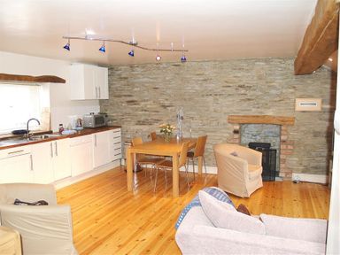 A kitchen and dining area with a wooden table and chairs stone wall and fireplace at Stable Cottage Cardigan in Cardigan Ceredigion