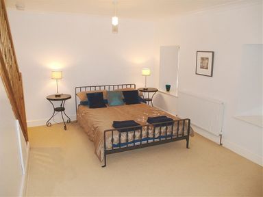 A bedroom with a bed side tables with lamps and stairs on the side at Stable Cottage Cardigan