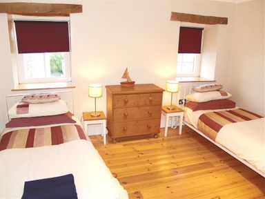 A bedroom with two single beds next to wooden dressers and two windows at Stable Cottage Cardigan