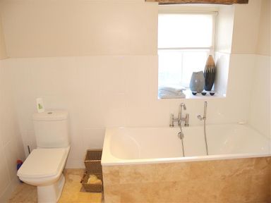 A bathroom with a toilet a bathtub a window with vases and towels on the sill at Stable Cottage Cardigan in Cardigan Ceredigion
