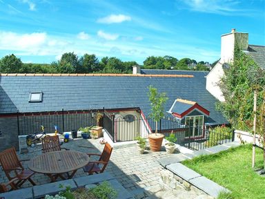 An outdoor patio area with wooden table and chairs potted plants toys and a slate roof at Stable Cottage Cardigan in Cardigan Ceredigion