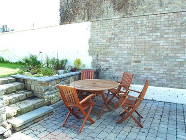 An outdoor patio area with a round wooden table and four wooden chairs stone steps and a rock wall garden at Stable Cottage Cardigan in Cardigan Ceredigion