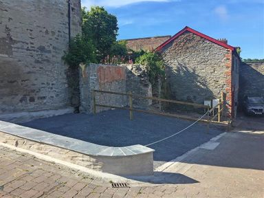 An outdoor space with stone walls a gravel area bordered by wooden railings and a parked car at Stable Cottage Cardigan in Cardigan Ceredigion