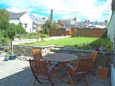 A garden with a wooden table and four chairs on a paved patio at Stable Cottage in Cardigan Ceredigion