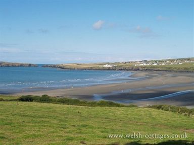 A coastal landscape with a bay sandy shore grassy foreground and houses on the hills at Stable Cottage in Cardigan Ceredigion