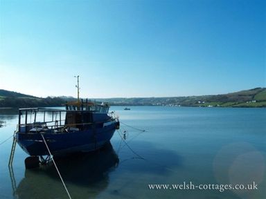 A blue boat moored on calm water with hills and houses in the background at Stable Cottage in Cardigan Cardigan Ceredigion