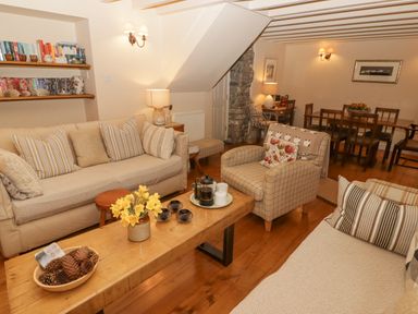 A living room with couches a wooden coffee table bookshelves and a dining table at 1 Cheriton Row Carew Cheriton Nr Tenby Pembrokeshire