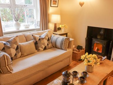 A living room with a sofa pillows a coffee table flowers a lamp and a fireplace at 1 Cheriton Row in Carew Cheriton Nr Tenby Pembrokeshire