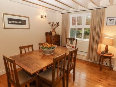 A dining room with a wooden table and chairs a basket with flowers on the table a window with curtains and a side table with a lamp at 1 Cheriton Row Carew Cheriton Nr Tenby Pembrokeshire