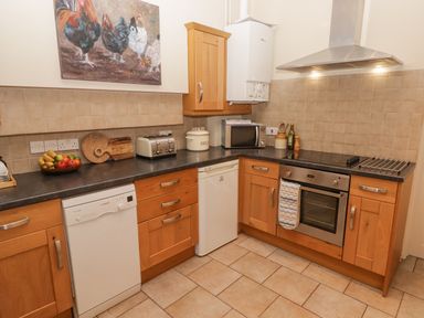 A kitchen with wooden cabinets a dishwasher a microwave an oven a toaster and a bowl of fruit at 1 Cheriton Row Carew Cheriton Nr Tenby Pembrokeshire