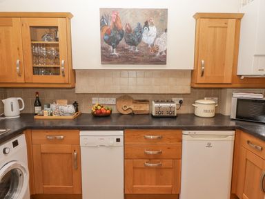 A kitchen with wooden cabinets a fruit bowl a toaster a bread container and a painting of chickens above the counter at 1 Cheriton Row Carew Cheriton Nr Tenby Pembrokeshire