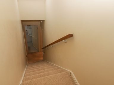 A carpeted staircase with a wooden handrail leading down to a hallway with an open door showing a sink in a bathroom at 1 Cheriton Row Carew Cheriton Nr Tenby Pembrokeshire
