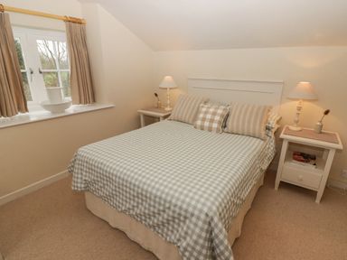 A bedroom with a double bed, two bedside tables with lamps, a window with curtains and a washbasin on the windowsill at 1 Cheriton Row in Carew Cheriton Nr Tenby Pembrokeshire