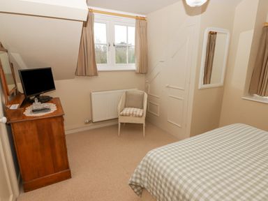 A bedroom with a bed covered in checkered bedding a wooden dresser with a television a chair and windows at 1 Cheriton Row Carew Cheriton Nr Tenby Pembrokeshire