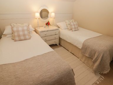 A bedroom with two single beds a bedside table with lamps a round mirror and cushions at 1 Cheriton Row Carew Cheriton Nr Tenby Pembrokeshire