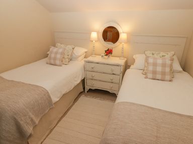 A bedroom with two single beds and a nightstand with lamps and a round mirror at 1 Cheriton Row Carew Cheriton Nr Tenby Pembrokeshire