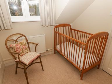 A small room with a wooden crib and a wooden chair with two cushions near a window at 1 Cheriton Row Carew Cheriton Nr Tenby Pembrokeshire