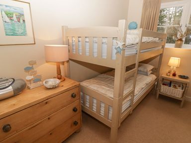 A bedroom with bunk beds a wooden dresser with a lamp and decorative fish a bedside table with a lamp and books a window with curtains at 1 Cheriton Row Carew Cheriton Nr Tenby Pembrokeshire
