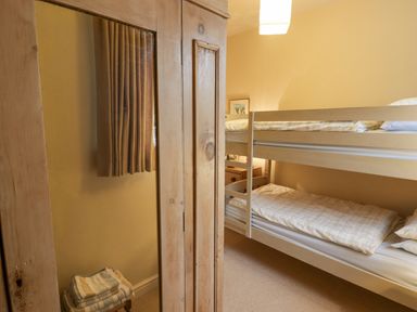 A bedroom with bunk beds a wooden wardrobe with a mirror folded towels on a stool and curtains at 1 Cheriton Row Carew Cheriton Nr Tenby Pembrokeshire