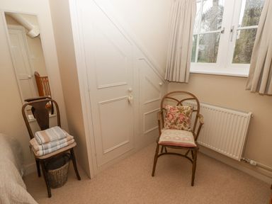 A bedroom corner with two wooden chairs one with folded blankets and a basket under it the other with cushions near a window and radiator at 1 Cheriton Row Carew Cheriton Nr Tenby Pembrokeshire