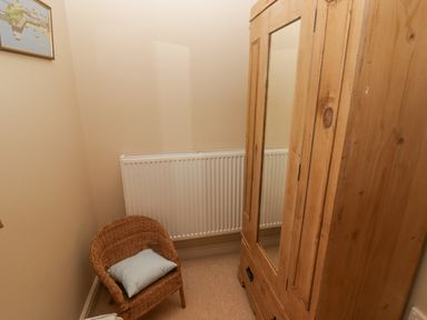 A small room with a wooden wardrobe with a mirror a wicker chair with a cushion a radiator and a framed picture on the wall at 1 Cheriton Row Carew Cheriton Nr Tenby Pembrokeshire