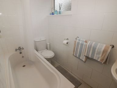 A bathroom with a bathtub toilet two towels on a towel rack and decorative items on a window ledge at 1 Cheriton Row Carew Cheriton Nr Tenby Pembrokeshire