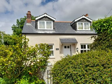 A cottage with two dormer windows and white door behind bushes at 1 Cheriton Row Carew Cheriton Nr Tenby Pembrokeshire